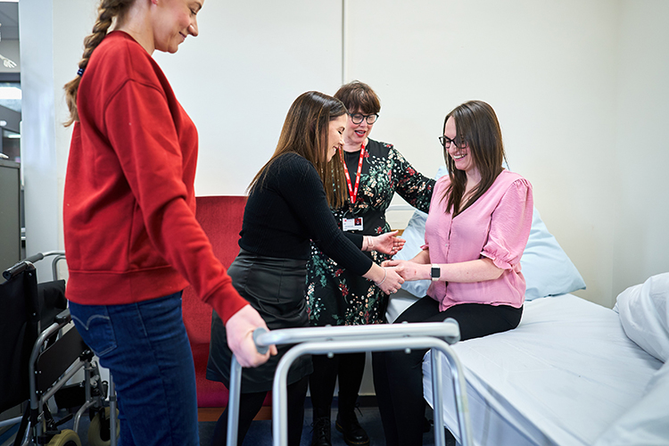 students helping another student on a bed with a walker