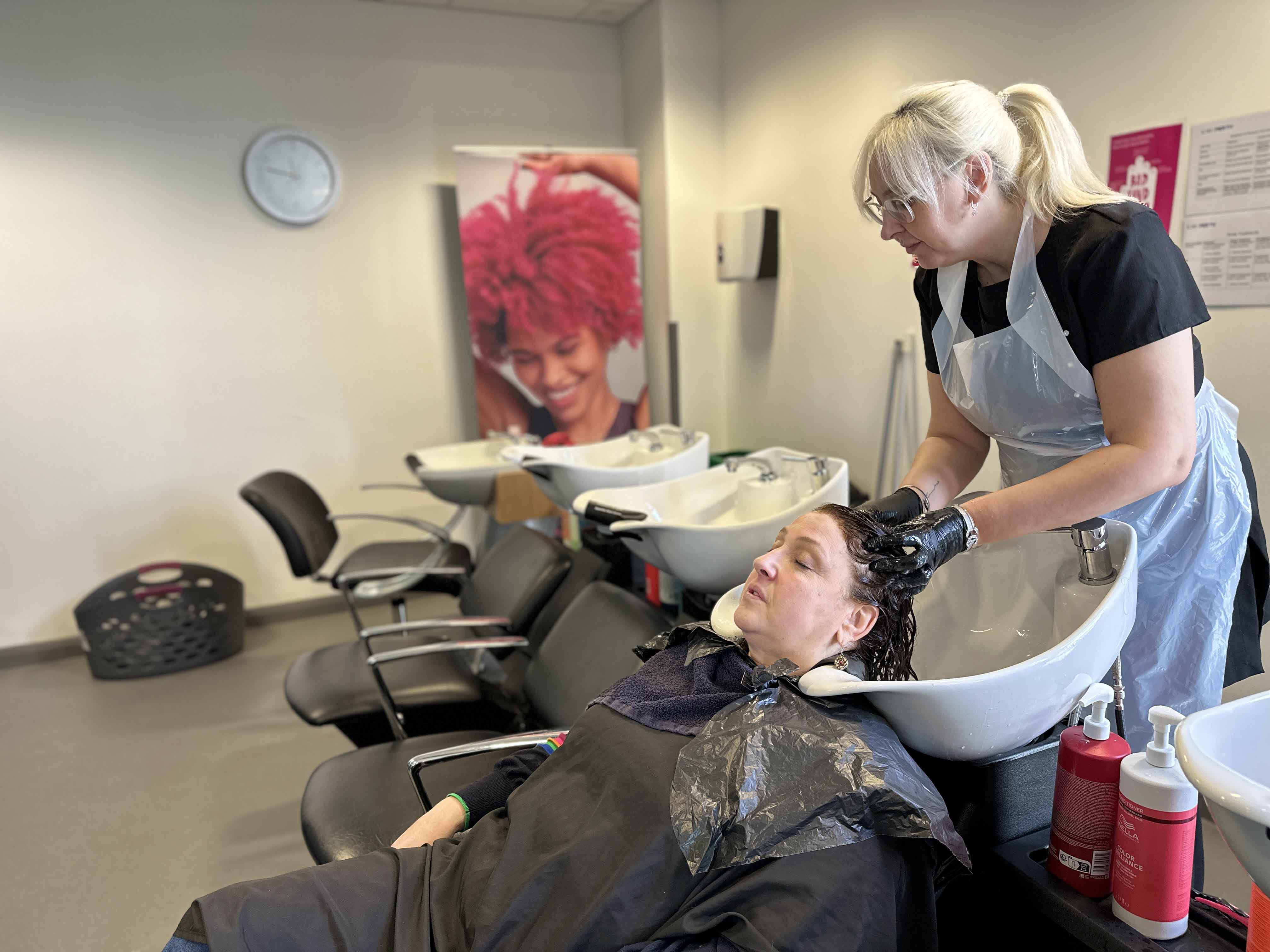 A female washing another female's hair in hairdressing sink in salon setting A female washing another female's hair in hairdressing sink in salon setting