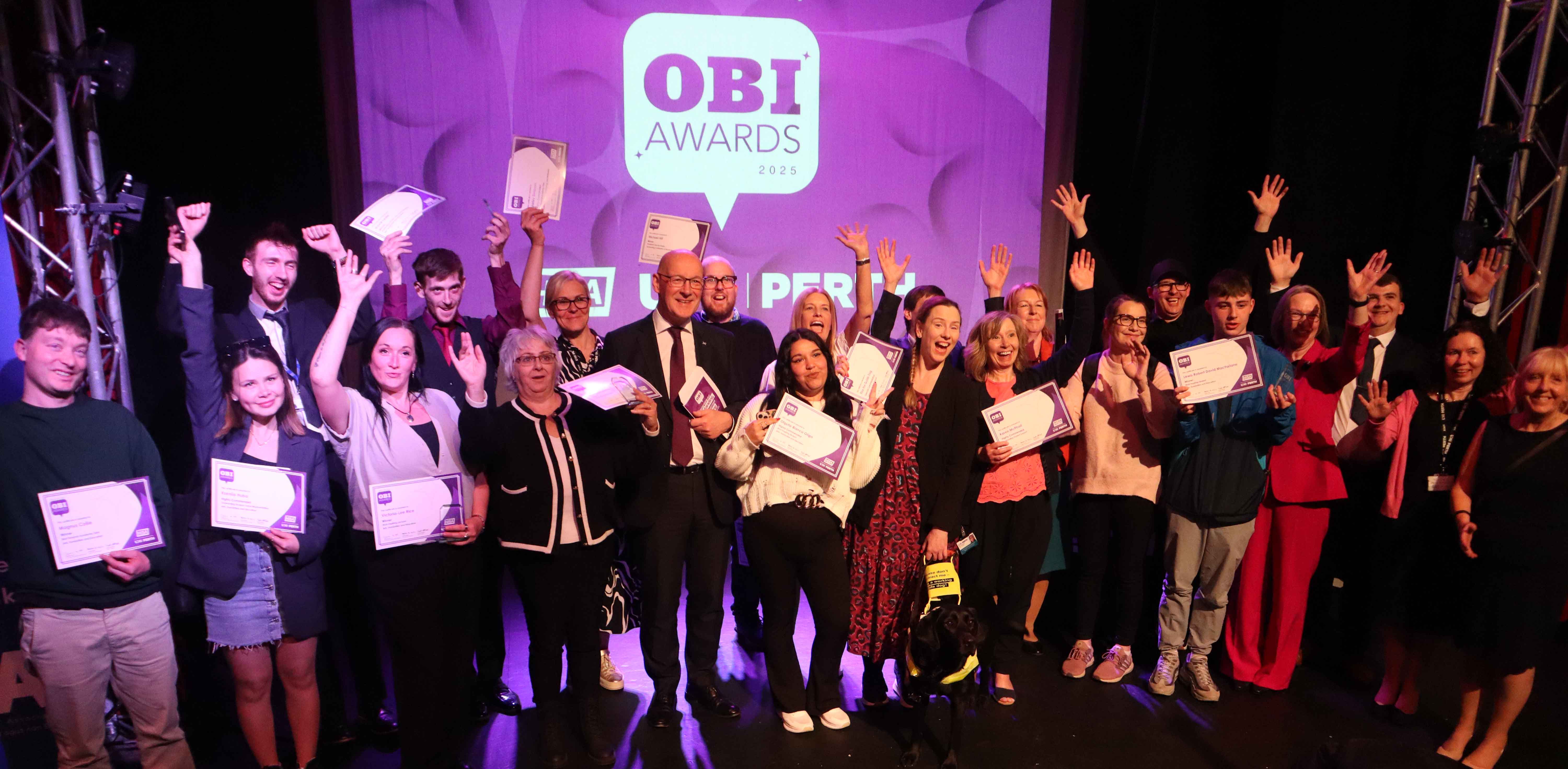 A group of staff and students waving their hands in the air to celebrate winning an OBI award