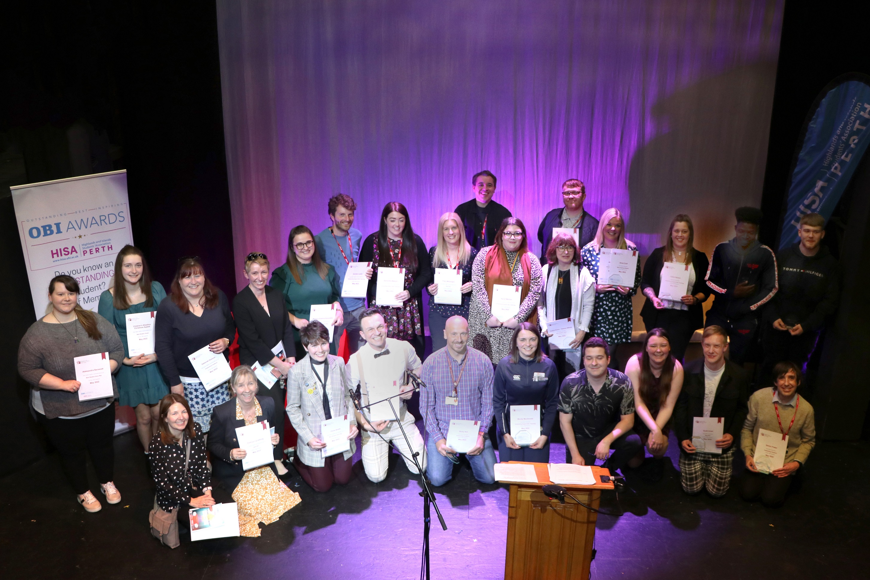 A group of people holding trophies and certificates smiling