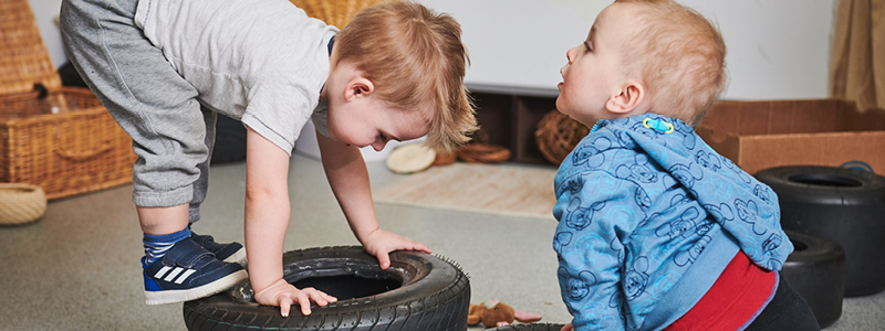 2 nursery kids playing on a small tyre