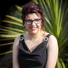 tracey standing in a black dress with a green leaf background