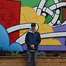 gregor standing in the wellness garden on campus with the piece of art he made for it