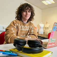 lucas in the vis comm classroom with a laptop and pair of headphones in front of him