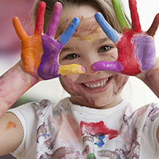 child holding up their hands covered in bright paint