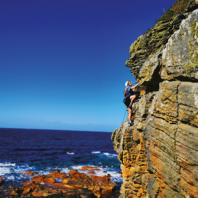 student climbing an outdoor cliff with the sea in the background student climbing an outdoor cliff with the sea in the background