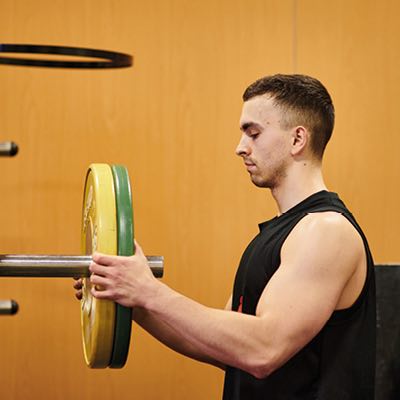 Student adding wieghlifting plates to a weightlifting bar on a squat rack