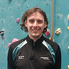 cameron standing in front of the climbing wall at the asw